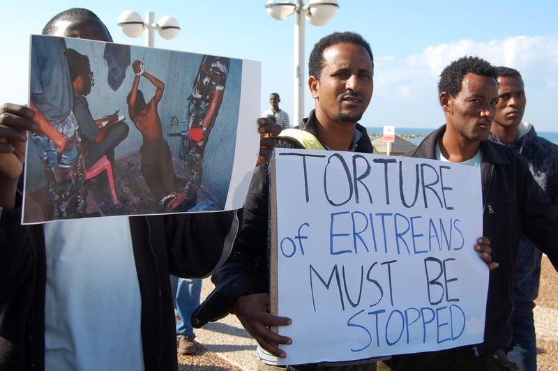 Men hold signs protesting the torture of Eritreans