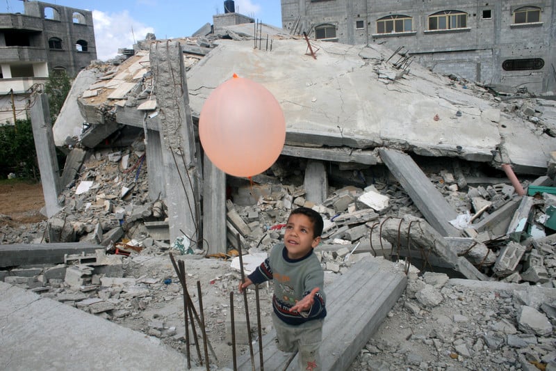 Boy plays with balloon amongst rubble of destroyed building
