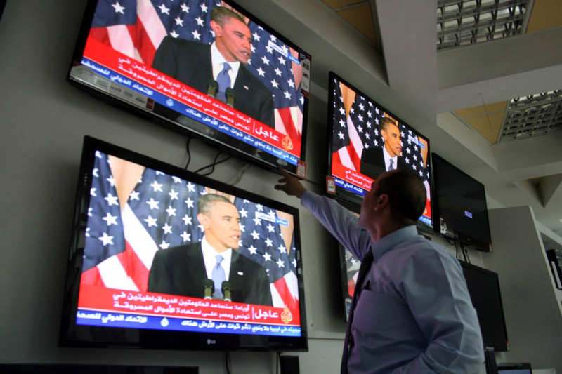 Man points at television screens showing Barack Obama