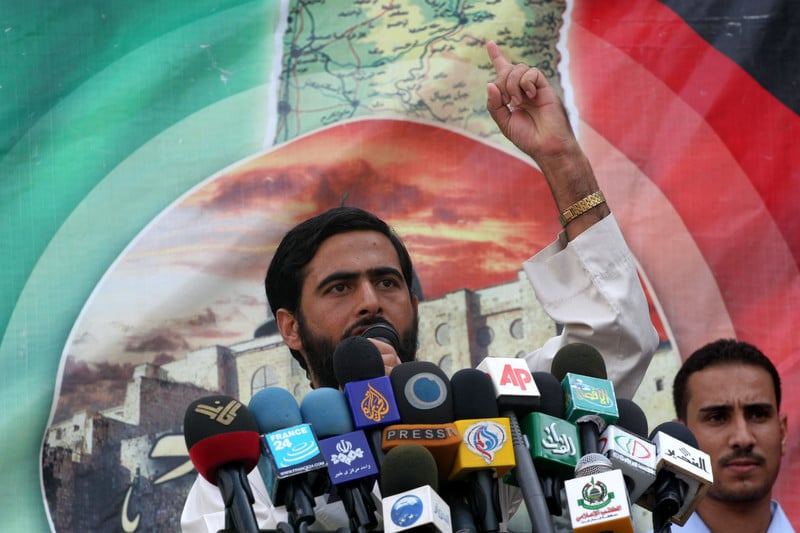 Mushir al-Masri gestures with his left hand while speaking into several microphones