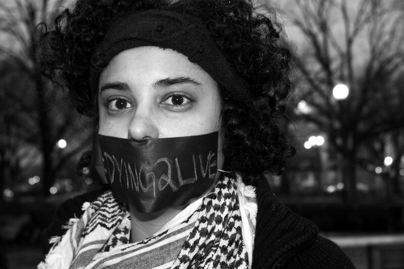 Protester wearing kuffiyeh has mouth covered with fabric reading &quot;dying2live&quot;