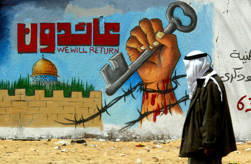 Man walks by mural of fist holding key reading "We will return" in Arabic and English