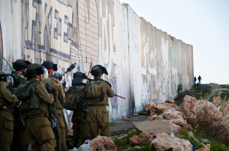 Heavily armed Israeli soldiers in front of grafittied concrete wall