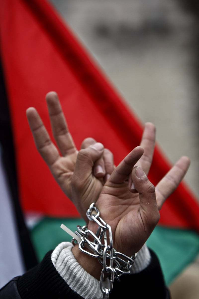 Close-up on hands in chains making &quot;v&quot; for victory sign with Palestinian flag in background