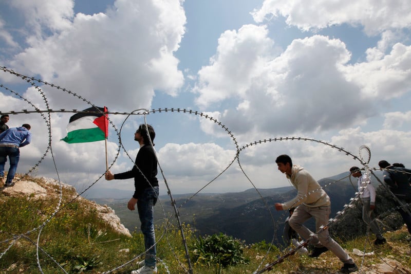 Young men and barbed wire in foreground with landscape of northern Palestine in background