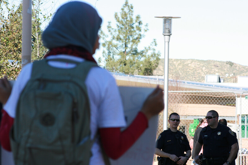 Woman protester holding sign in foreground with police in background