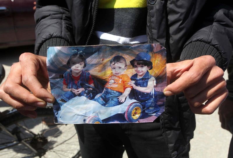 Man displays worn portrait photograph of three small children killed in fire