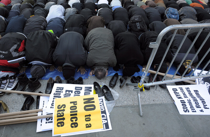 Men pray near picket signs protesting the targeting of Muslims