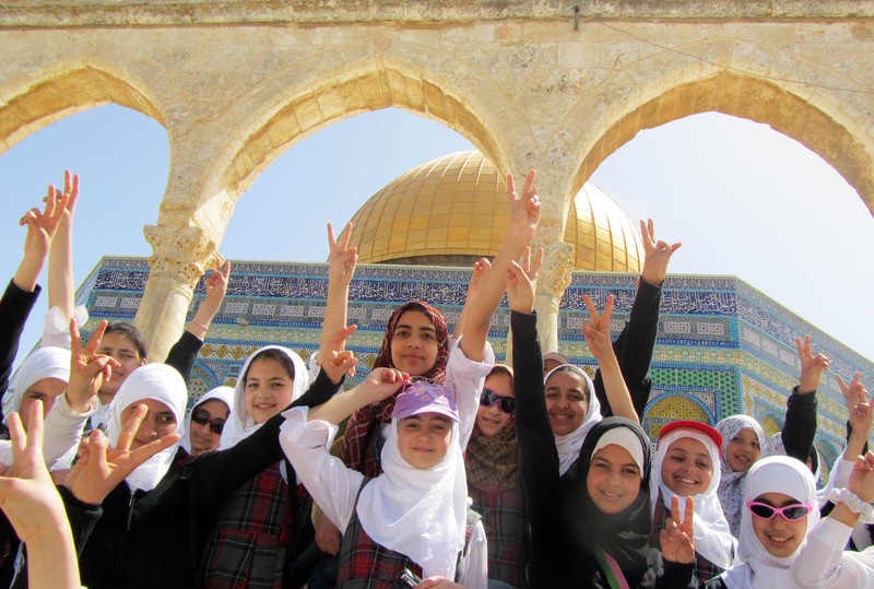 Girls smile and raise &quot;victory&quot; hand gesture in front of Dome of the Rock