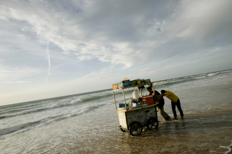 Two people push cart on the shore of the sea