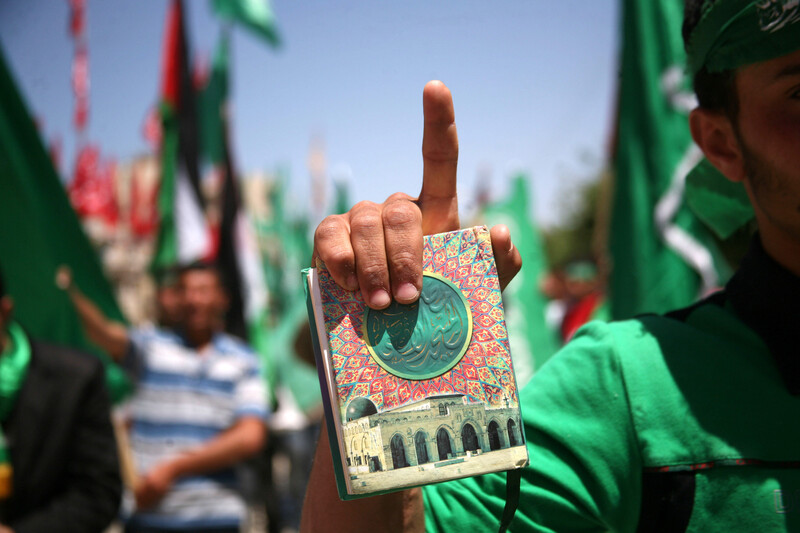 Demonstrator holds Quran and points toward sky