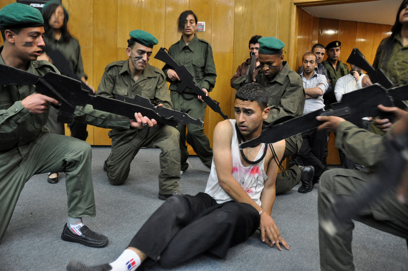 Actors dressed as Israeli soldiers point fake guns at cowering young man