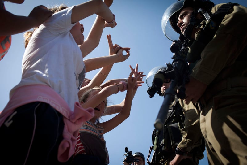 Girls shout and display victory hand gesture to armed Israeli soldiers