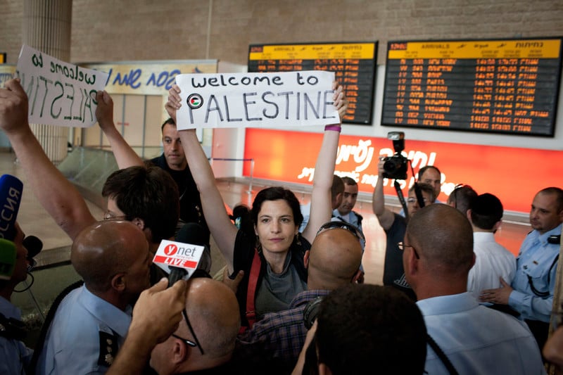 Activists display signs reading &quot;Welcome to Palestine,&quot; surrounded by media