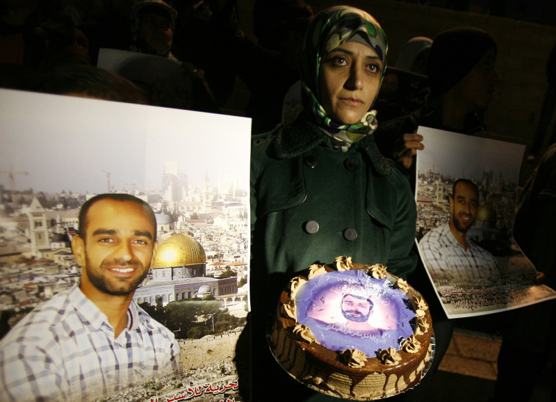 Woman holds a cake, surrounded by posters of prisoner
