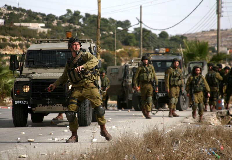 Soldier next to jeep throwing grenade. More soldiers nearby.