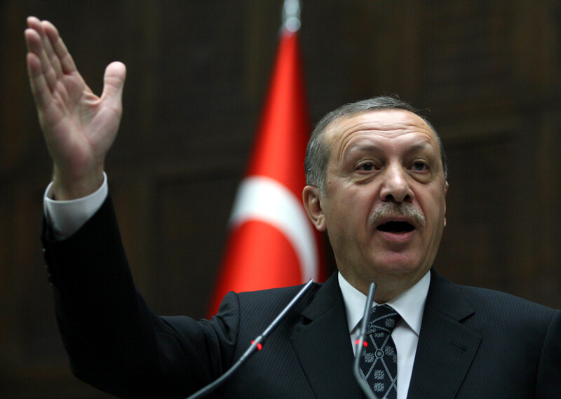 Turkish prime minister seen gesturing with hand in front of flag of Turkey