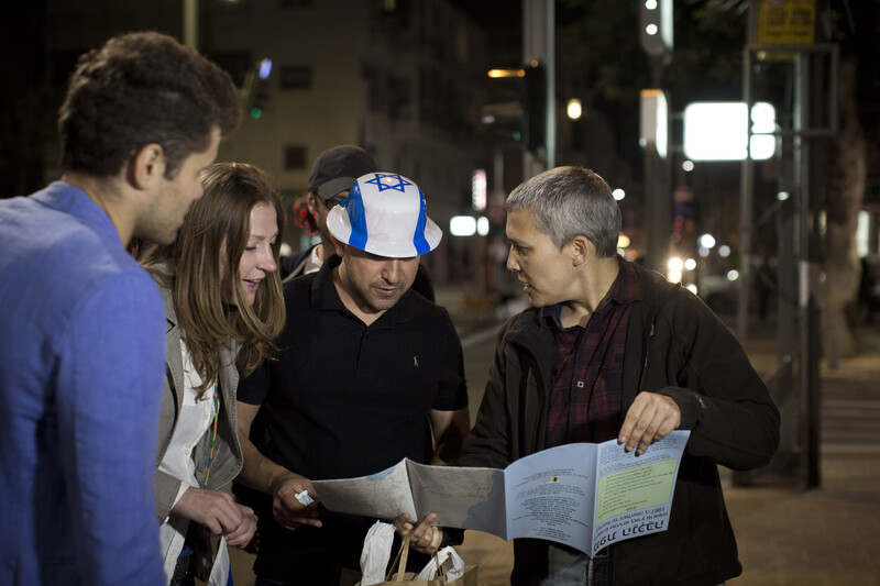 Group including man wearing flag of Israel hat looks at map