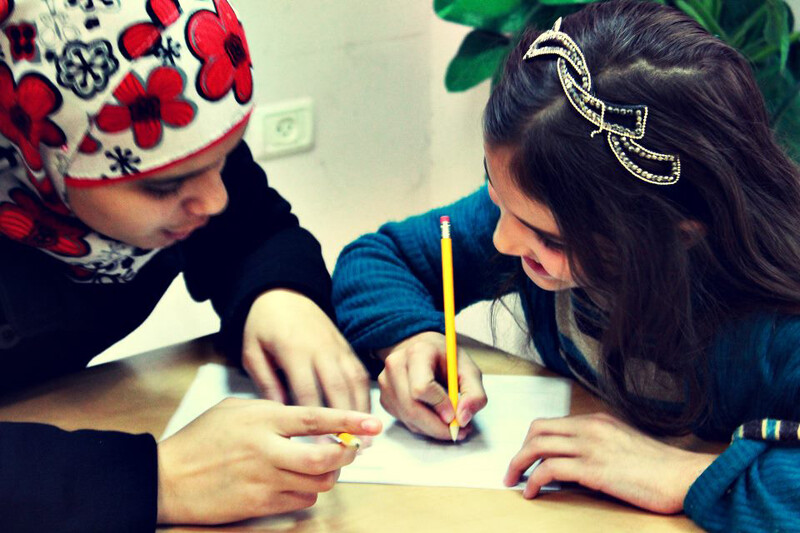 Young woman speaks to girl drawing