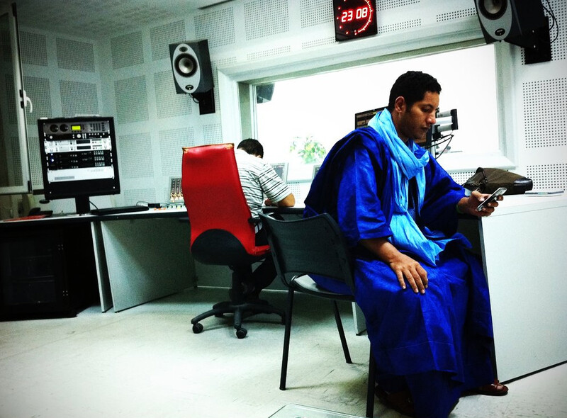 Man wearing blue robe looks at his phone in a radio station suite