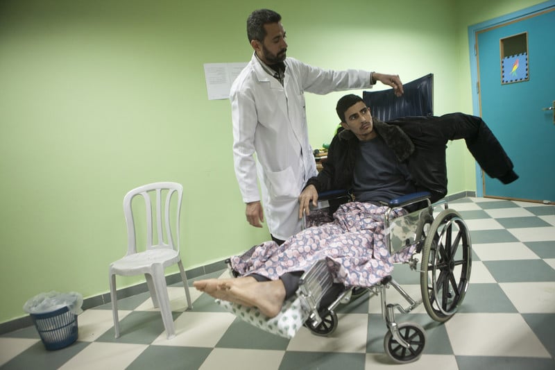 Medical aide stands next to man using wheelchair