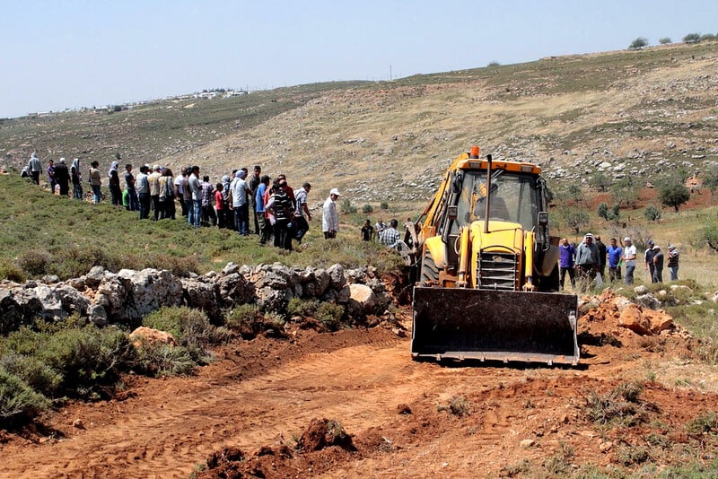 Landscape scene shows crowd of people next to bulldozer