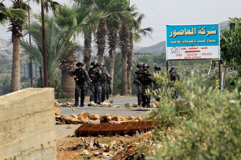 Heavily armed soldiers stand in front of palm trees