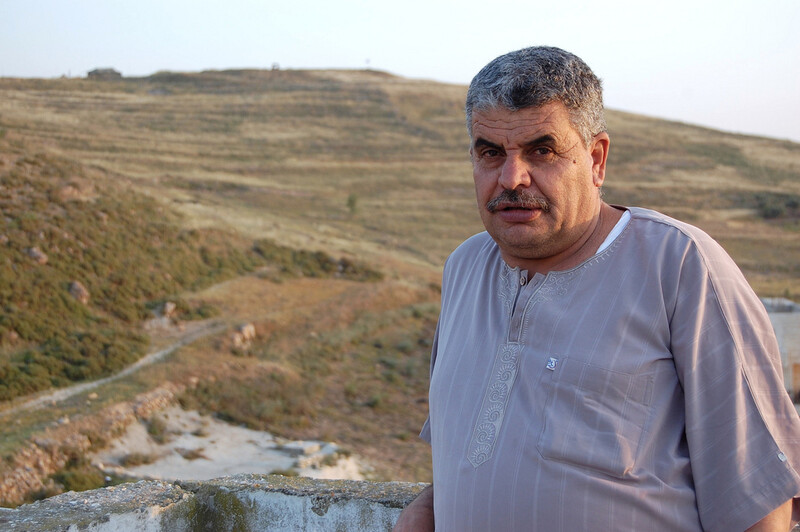 Man stands with Israeli outpost on hill in background