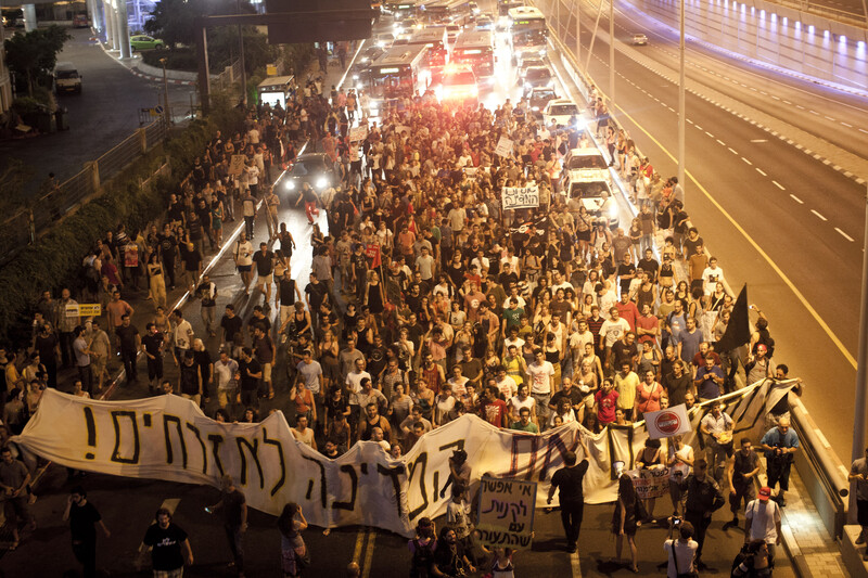 Protesters march down a highway carrying banners and signs