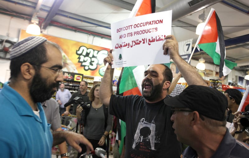 Man holds up sign reading &quot;Boycott occupation and its products&quot; in Arabic and English