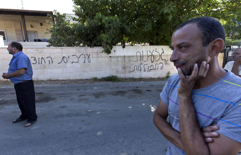 Men stand near wall sprayed-painted with graffiti