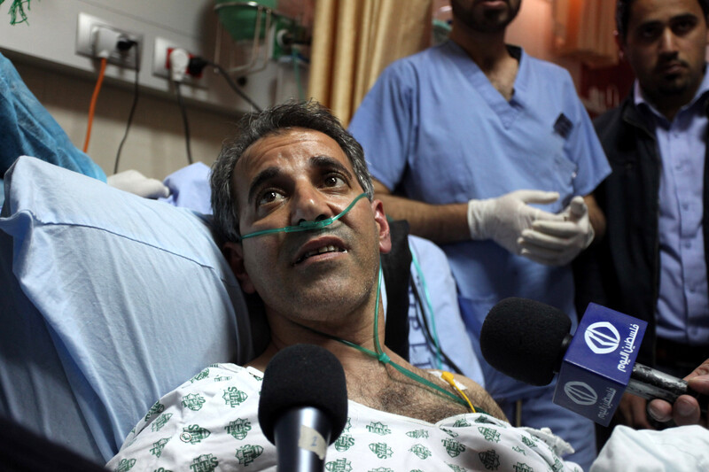 Man on hospital bed surrounded by microphones