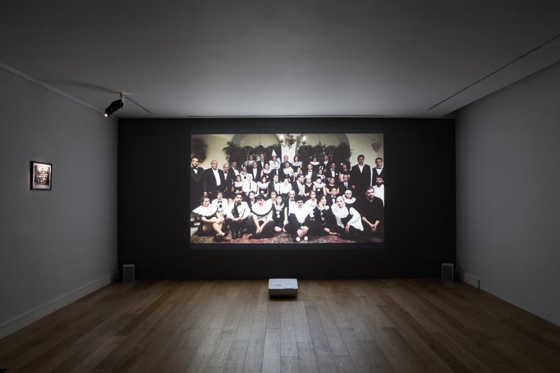 Installation view of projection of posed group of people in masquerade costume