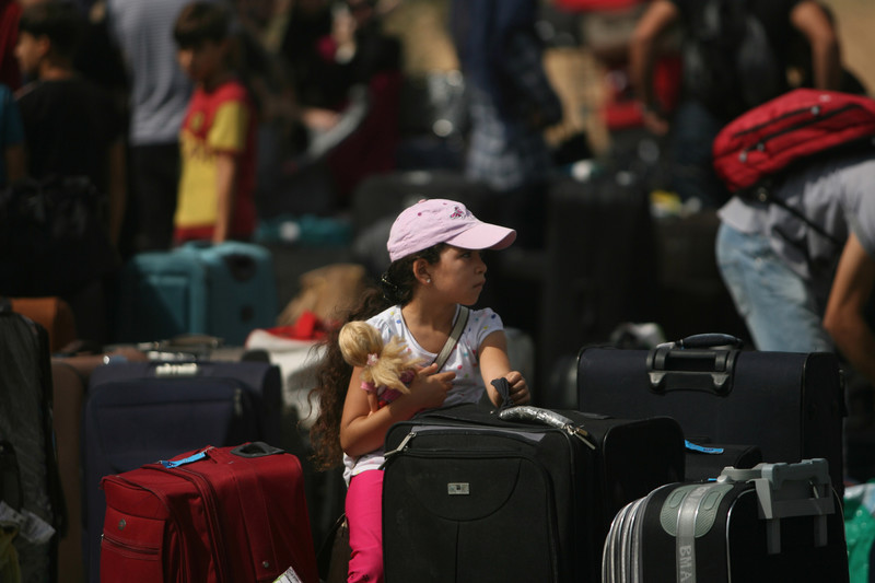 Girl holding doll sits amidst suitcases