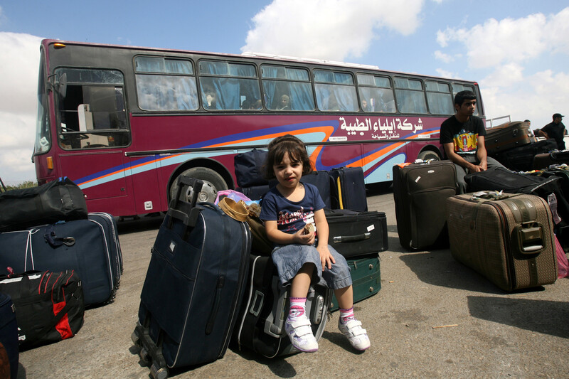 Girl sits amid suitcases in front of bus