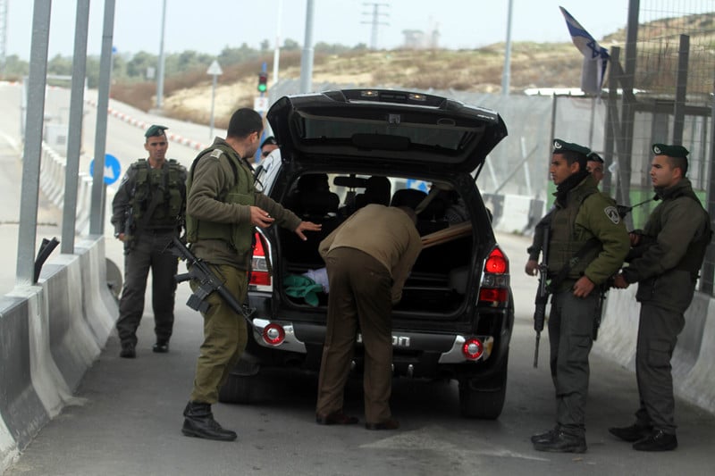 Man opens boot of car as soldiers look on