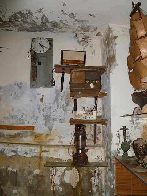 Vintage radios sit on shelves mounted on water-damaged wall