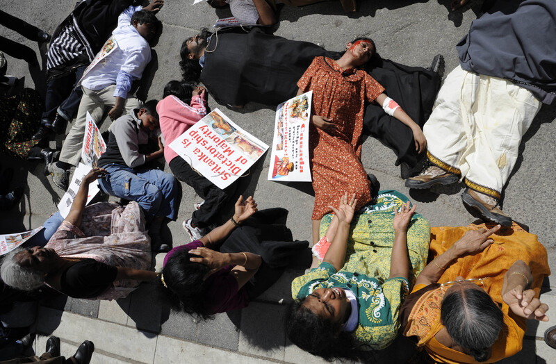 Women wearing mock blood lie on ground surrounded by other seated women