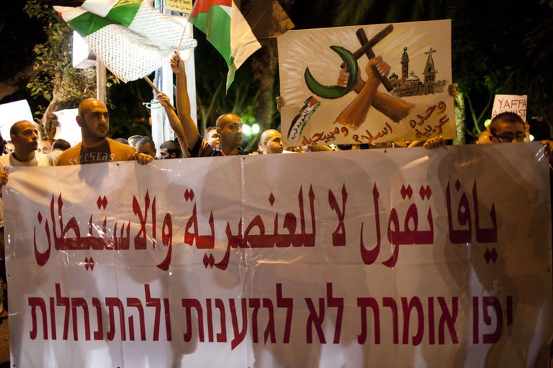 Men carry banner reading Yaffa says no to racism and settlements in Arabic and Hebrew