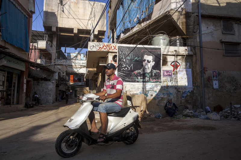 Scene shows youth on scooter riding past wall covered with poster and graffiti