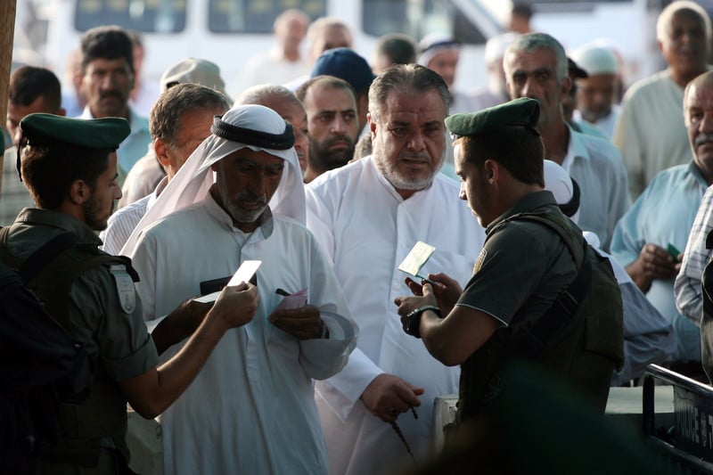Israeli soldiers inspect the IDs of Palestinian men at a checkpoint