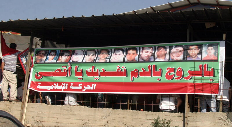 Arabic-language banner features the portraits of 13 males shot by Israeli police