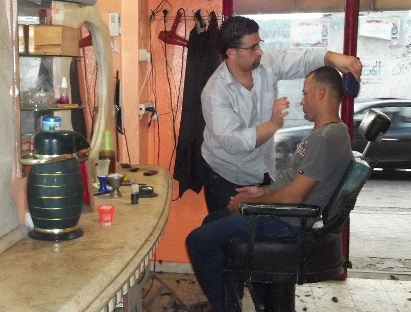 Young man grooms another man sitting in barber shop chair