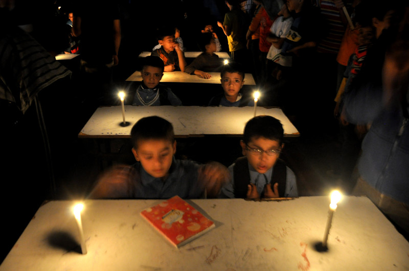 Boys sit at school desks in room lit with candles
