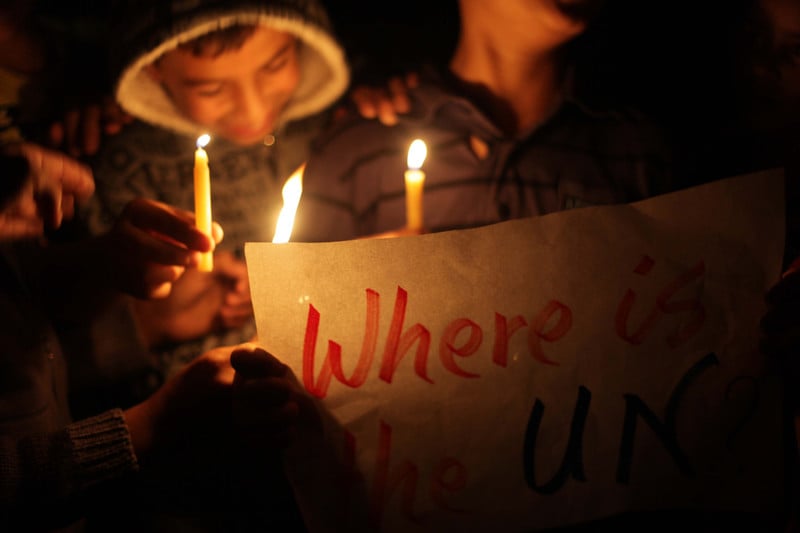 Smiling boy holds candle and sign reading: Where is the UN