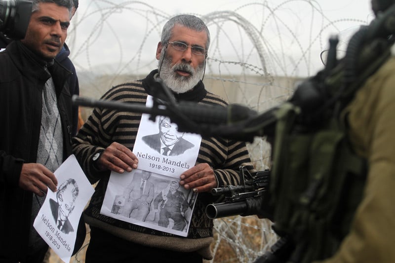 Middle-aged man holds photo of Mandela in front of heavily armed Israeli soldier