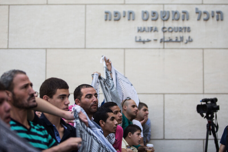 Men wearing checkered scarves hold banners outside court house