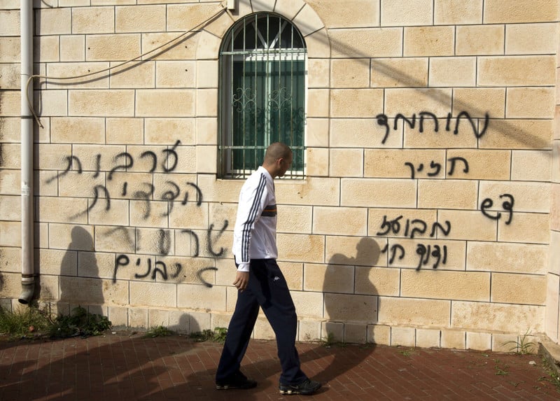 Man walks in front of stone wall spray painted with Hebrew graffiti