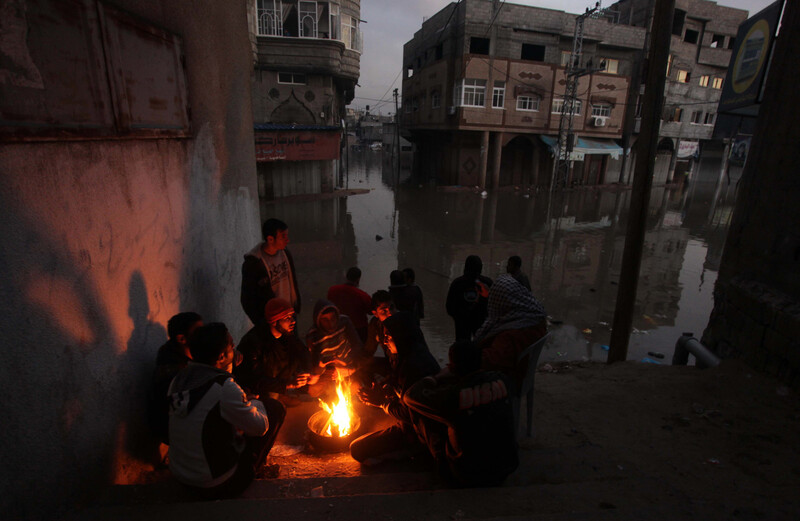 Men sit by campfire in flooded urban area