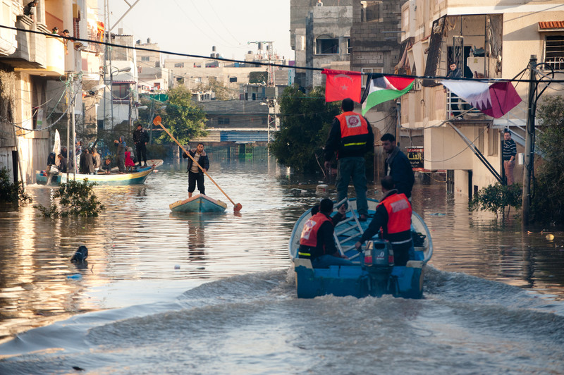 Men in small boats paddle through flooded urban area